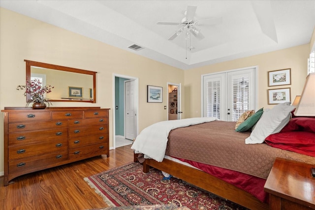 bedroom featuring wood finished floors, visible vents, access to exterior, french doors, and a raised ceiling