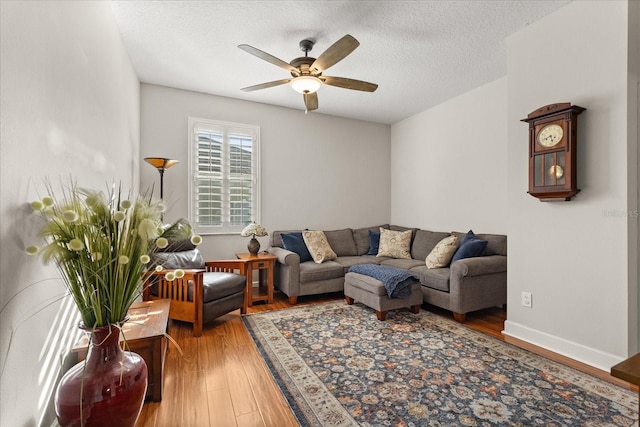 living room with a textured ceiling, wood finished floors, a ceiling fan, and baseboards