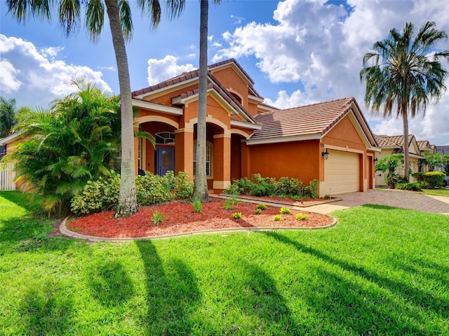 mediterranean / spanish home featuring decorative driveway, a tile roof, stucco siding, an attached garage, and a front yard