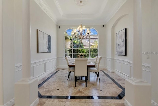 dining room with decorative columns, ornamental molding, a raised ceiling, a decorative wall, and a notable chandelier