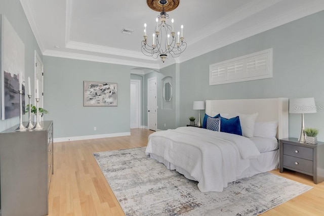 bedroom featuring light wood finished floors, crown molding, and a raised ceiling