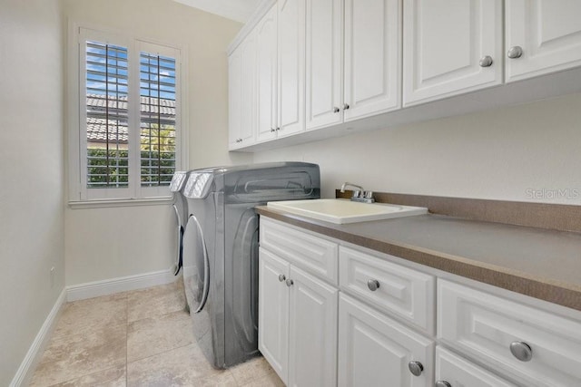 clothes washing area featuring a sink, cabinet space, separate washer and dryer, light tile patterned floors, and baseboards