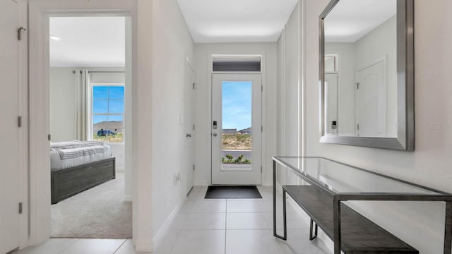 doorway featuring light tile patterned floors, baseboards, and light colored carpet