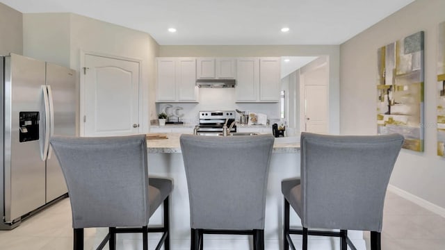 kitchen with appliances with stainless steel finishes, a kitchen breakfast bar, a kitchen island with sink, light countertops, and under cabinet range hood