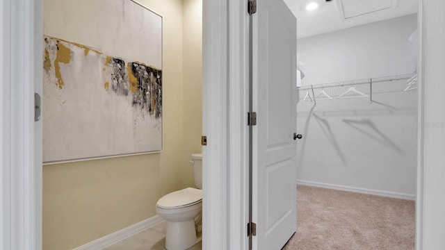 bathroom with a spacious closet, toilet, and baseboards