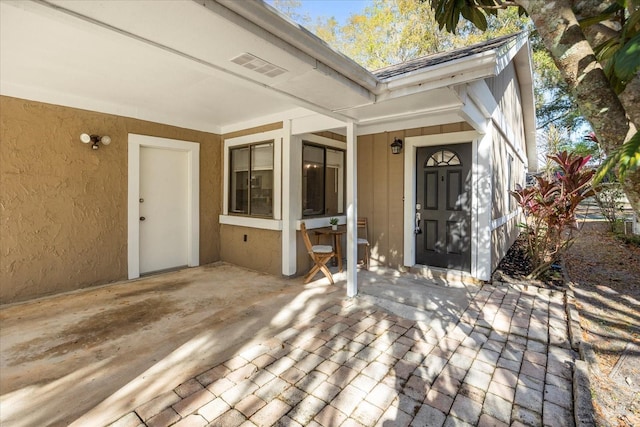 view of exterior entry with stucco siding, visible vents, and a patio