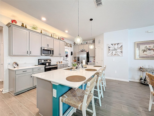 kitchen with a center island with sink, visible vents, appliances with stainless steel finishes, a breakfast bar area, and gray cabinetry