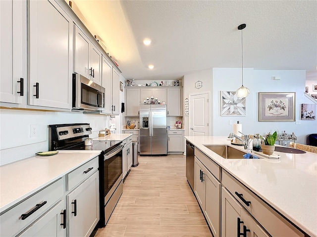 kitchen featuring light wood-style flooring, a sink, light countertops, appliances with stainless steel finishes, and decorative light fixtures