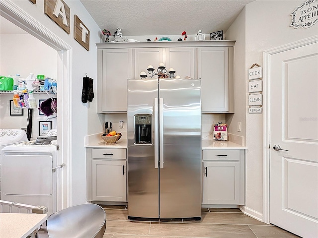 kitchen featuring stainless steel fridge with ice dispenser, light countertops, washer and dryer, wood finish floors, and a textured ceiling