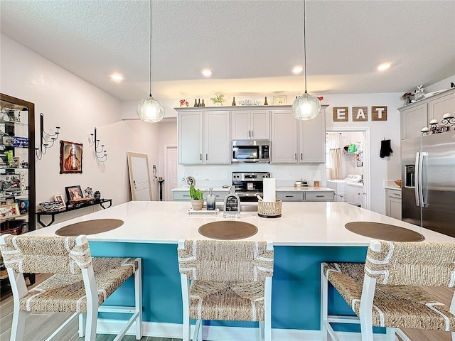 kitchen featuring stainless steel appliances, a breakfast bar area, washing machine and dryer, and light countertops