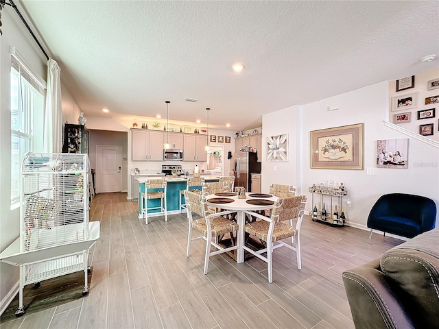 dining area featuring light wood-style flooring, visible vents, and a textured ceiling