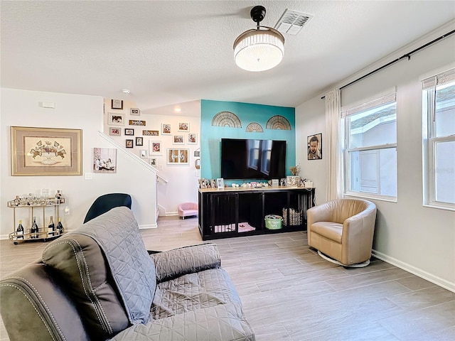 living room featuring a textured ceiling, light wood finished floors, visible vents, and baseboards