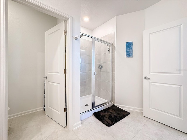 full bathroom with a stall shower, tile patterned flooring, toilet, and baseboards