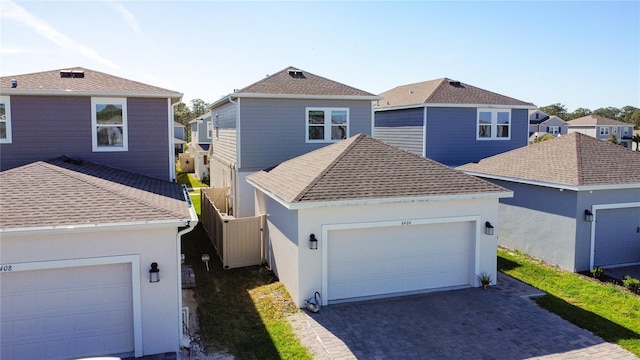 traditional home with a shingled roof, an attached garage, fence, decorative driveway, and stucco siding