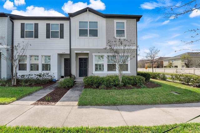 townhome / multi-family property with fence, board and batten siding, and a front yard