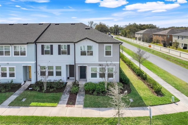 townhome / multi-family property with roof with shingles and a front lawn