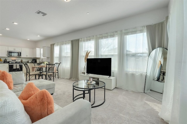 living area with recessed lighting, visible vents, and light colored carpet