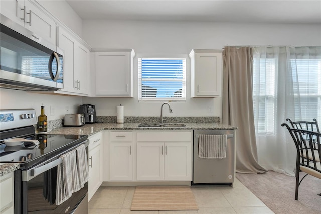 kitchen with appliances with stainless steel finishes, white cabinets, light tile patterned flooring, and a sink