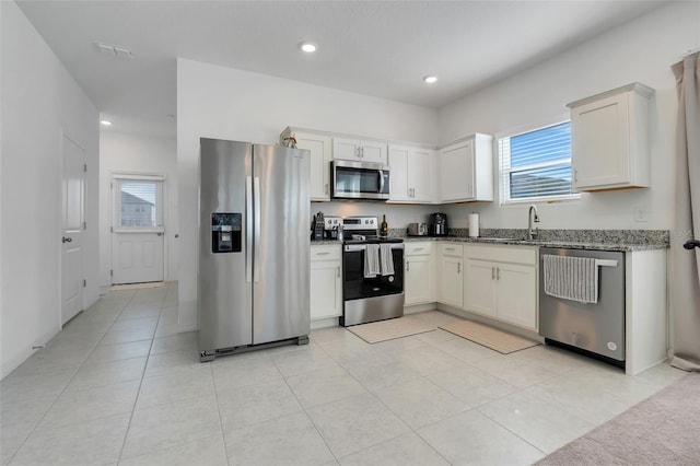 kitchen with stone counters, light tile patterned floors, appliances with stainless steel finishes, and white cabinets