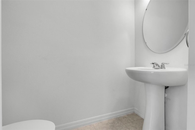 half bath with toilet, baseboards, and tile patterned floors