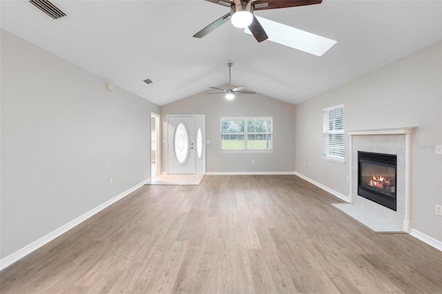 unfurnished living room with light wood finished floors, vaulted ceiling with skylight, visible vents, and a tiled fireplace