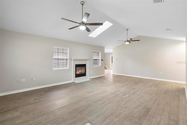 unfurnished living room featuring a fireplace with flush hearth, lofted ceiling with skylight, ceiling fan, wood finished floors, and baseboards