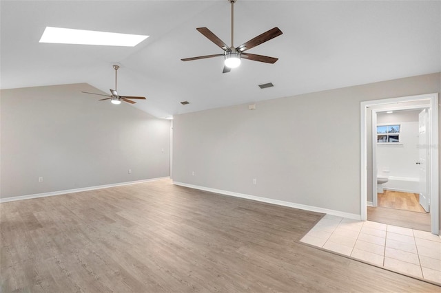 spare room featuring light wood finished floors, vaulted ceiling with skylight, visible vents, baseboards, and ceiling fan