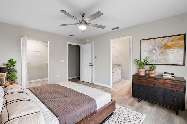 bedroom with light wood finished floors, connected bathroom, visible vents, and baseboards