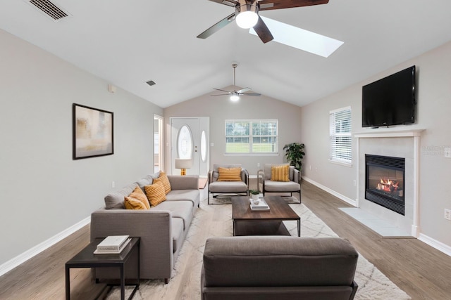 living area featuring lofted ceiling, light wood finished floors, a fireplace with flush hearth, and visible vents