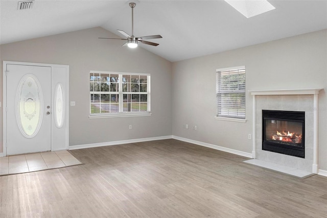 unfurnished living room with a fireplace, visible vents, ceiling fan, wood finished floors, and vaulted ceiling with skylight