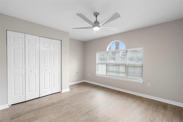 unfurnished bedroom featuring light wood-type flooring, ceiling fan, baseboards, and a closet