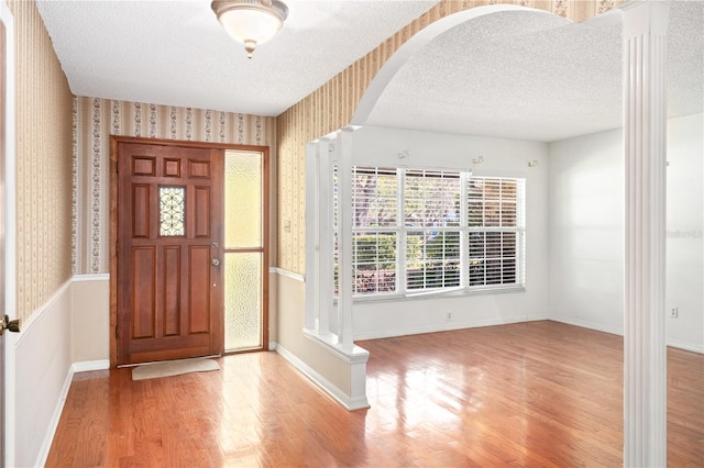 foyer entrance with arched walkways, a textured ceiling, wood finished floors, baseboards, and wallpapered walls