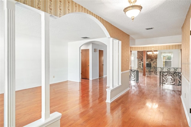 interior space with visible vents, light wood-style flooring, a textured ceiling, and wallpapered walls