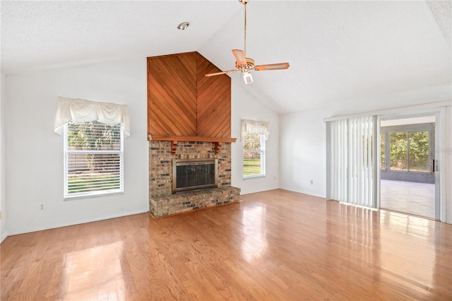 unfurnished living room featuring a ceiling fan, a brick fireplace, a textured ceiling, wood finished floors, and high vaulted ceiling