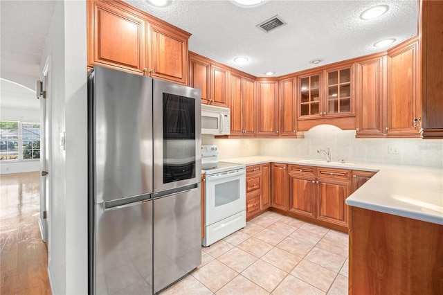 kitchen featuring brown cabinetry, white appliances, visible vents, and glass insert cabinets