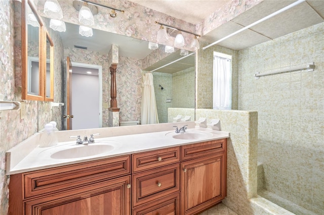 bathroom with a sink, wallpapered walls, double vanity, and tiled shower