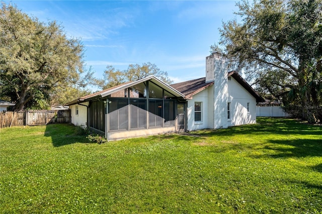 back of property featuring a lawn, a chimney, a fenced backyard, and a sunroom