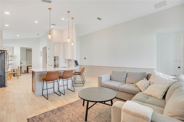 living area with visible vents, wainscoting, and light wood-type flooring