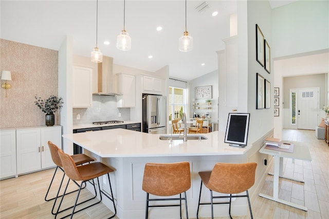 kitchen with visible vents, a sink, appliances with stainless steel finishes, a breakfast bar area, and wall chimney exhaust hood