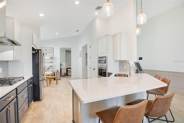 kitchen featuring visible vents, stainless steel appliances, a sink, light countertops, and wall chimney exhaust hood