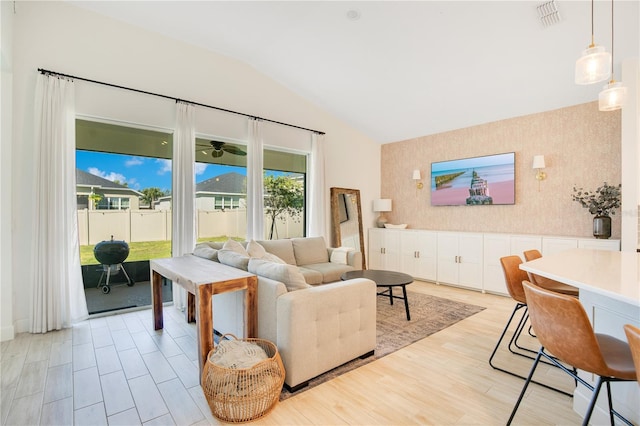 living area featuring wallpapered walls, lofted ceiling, visible vents, and light wood finished floors