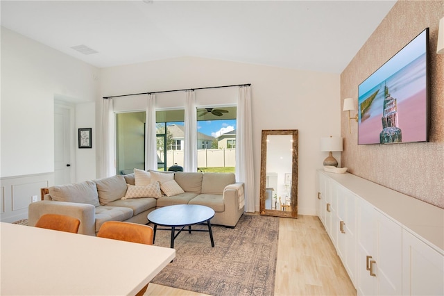 living room featuring visible vents, a wainscoted wall, vaulted ceiling, and light wood finished floors