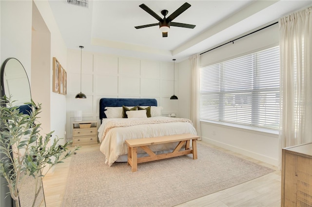 bedroom featuring a tray ceiling, baseboards, visible vents, and a ceiling fan