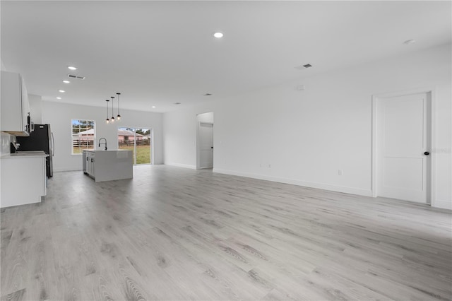 unfurnished living room featuring light wood-style flooring, recessed lighting, a sink, visible vents, and baseboards