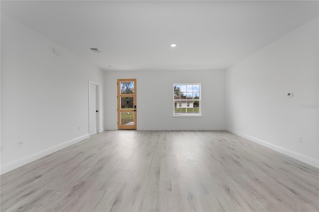 empty room with baseboards, visible vents, and light wood finished floors