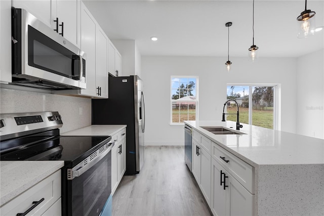 kitchen featuring a kitchen island with sink, a sink, light wood-style floors, appliances with stainless steel finishes, and tasteful backsplash