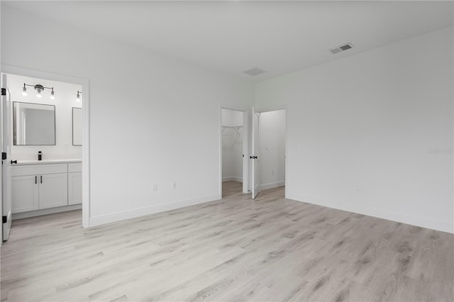 unfurnished bedroom with light wood-type flooring, baseboards, visible vents, and a walk in closet