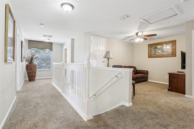 hall with attic access, visible vents, carpet flooring, and an upstairs landing