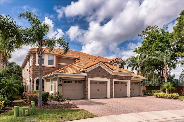 mediterranean / spanish-style home with a garage, decorative driveway, a tile roof, and stucco siding