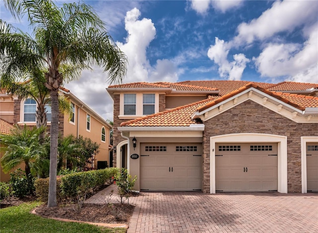 mediterranean / spanish home with decorative driveway, a tiled roof, an attached garage, and stucco siding